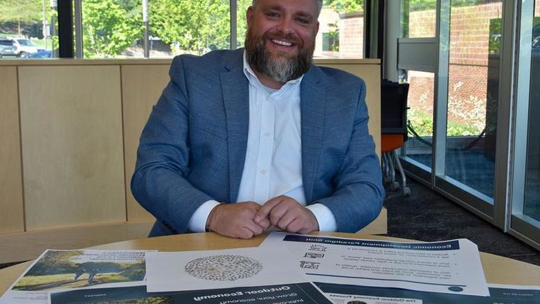 Bearded white male dressed in a suit showing off materials on the desk in front of him.