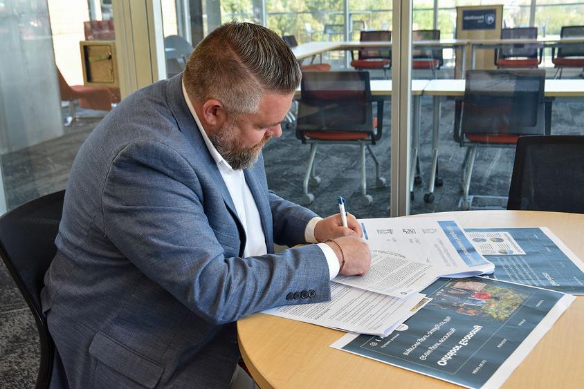 Man in a suit at a table writing on documents.